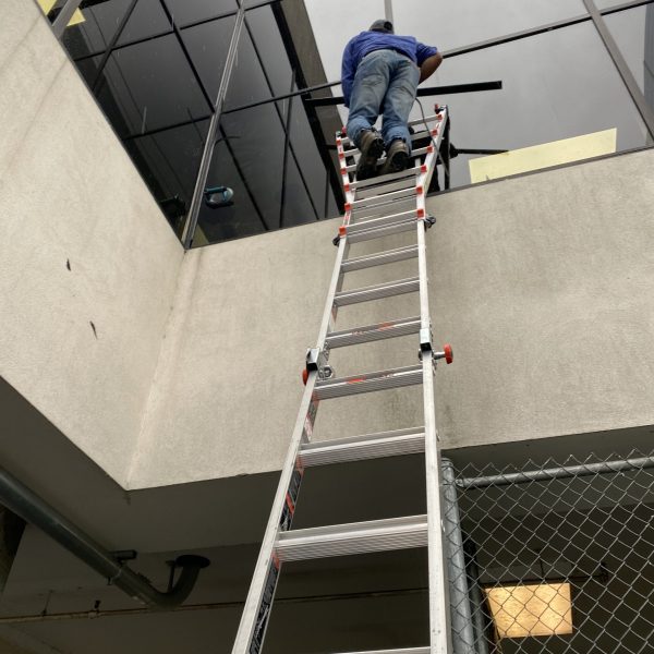 A team member using a ladder to reach windows that are high up.